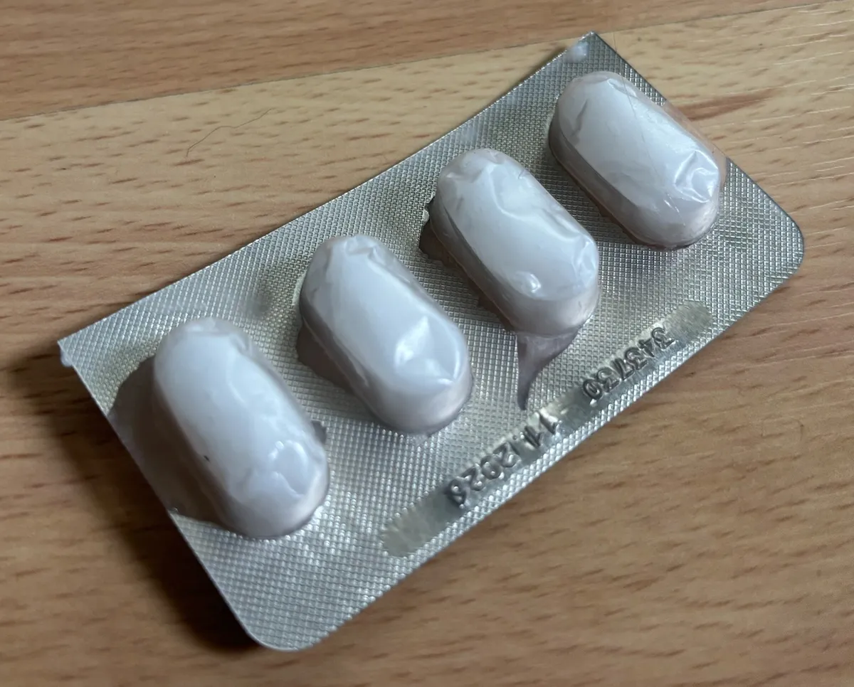 An empty pill blister pack on a wooden table, its four pockets filled with white coconut oil frozen into smooth pill shapes.
